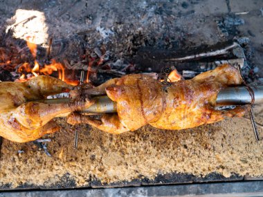 Barbekü başlıyor. Taze tavuklar kayın ağacı alevlerinin yanında döner. Arka planda tütsülenmiş tuğla duvar. Açık hava yemekleri..