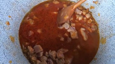 Şef, kebabı uzun tahta kaşıkla derin tencereye karıştırıyor. Lezzetli gulaş tabanı olarak güçlü soslu küçük parça domuz eti. Parti yemeği için güzel bir hazırlık..