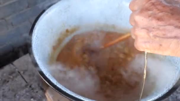 木製のスプーンは鍋に沸騰した赤い肉料理を混合しています 直火で調理する — ストック動画