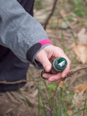 Geocaching container in hand. Woman  removes list from locating ampoule for geocatching  game. clipart