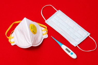 Üst görüntü fotoğrafı. Coronavirüs - 2019-nCoV, virüs konsepti. Beyaz cerrahi maske koruyucu elektronik termometre 42,5 C gösteriyor. Kırmızı arkaplan. Uzayı kopyala, taklit et..