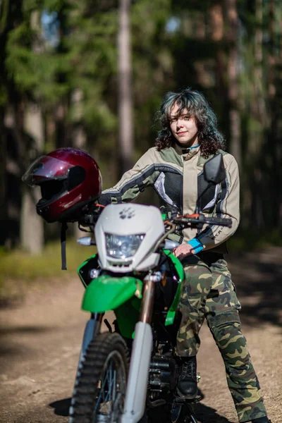 Motosikletli güzel bir kız, kıvırcık saçlı, genç bir kız, motosikletçi, motosikletçi için ekipman, güzel pozlar, çekicilik, motosiklet sürücüsü, konsept, aktif yaşam tarzı, dayanıklılık.