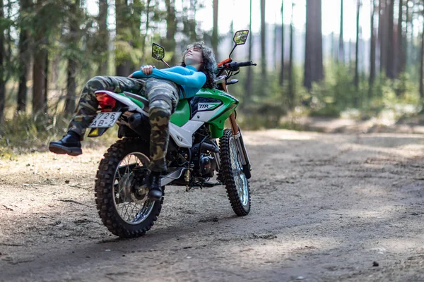 Motosikletli güzel bir kız, kıvırcık saçlı, genç bir kız, motosikletçi, motosikletçi için ekipman, güzel pozlar, çekicilik, motosiklet sürücüsü, konsept, aktif yaşam tarzı, dayanıklılık.