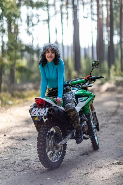 Motosikletli güzel bir kız, kıvırcık saçlı, genç bir kız, motosikletçi, motosikletçi için ekipman, güzel pozlar, çekicilik, motosiklet sürücüsü, konsept, aktif yaşam tarzı, dayanıklılık.