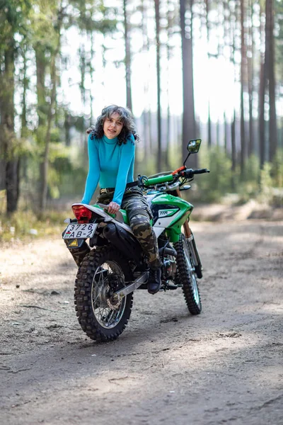 Motosikletli güzel bir kız, kıvırcık saçlı, genç bir kız, motosikletçi, motosikletçi için ekipman, güzel pozlar, çekicilik, motosiklet sürücüsü, konsept, aktif yaşam tarzı, dayanıklılık.