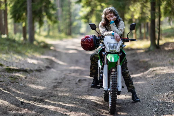 Motosikletli güzel bir kız, kıvırcık saçlı, genç bir kız, motosikletçi, motosikletçi için ekipman, güzel pozlar, çekicilik, motosiklet sürücüsü, konsept, aktif yaşam tarzı, dayanıklılık.