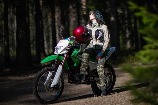 Motosikletli güzel bir kız, kıvırcık saçlı, genç bir kız, motosikletçi, motosikletçi için ekipman, güzel pozlar, çekicilik, motosiklet sürücüsü, konsept, aktif yaşam tarzı, dayanıklılık.