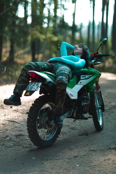 Motosikletli güzel bir kız, kıvırcık saçlı, genç bir kız, motosikletçi, motosikletçi için ekipman, güzel pozlar, çekicilik, motosiklet sürücüsü, konsept, aktif yaşam tarzı, dayanıklılık.