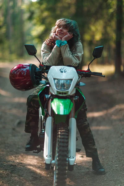 Motosikletli güzel bir kız, kıvırcık saçlı, genç bir kız, motosikletçi, motosikletçi için ekipman, güzel pozlar, çekicilik, motosiklet sürücüsü, konsept, aktif yaşam tarzı, dayanıklılık.