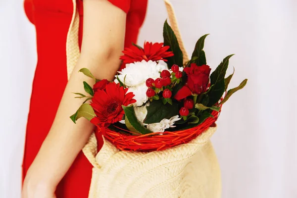 A girl in a red dress holds flowers.  Female hands hold a bouquet of flowers.  Red linen dress.  Beautiful bouquet with red and white flowers