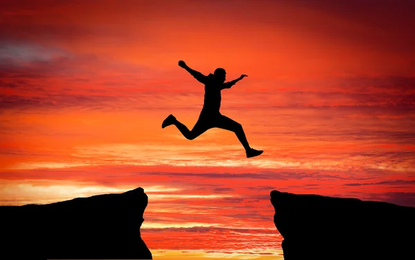 Man jumping across the gap from one rock to cling to the other. — Stock Photo, Image