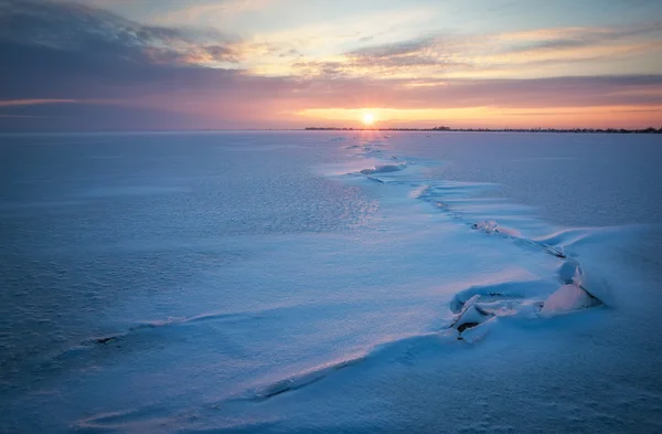 Vinterlandskap med frusen sjö, sprickor och solnedgång sky. — Stockfoto