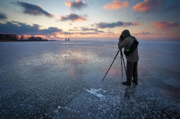 Фотограф фотографирует закат на замерзшей реке зимой — стоковое фото