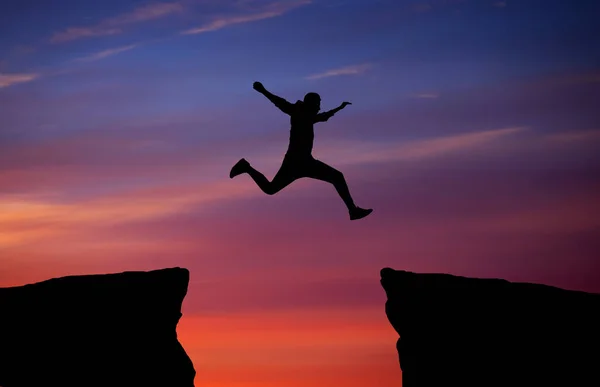 Hombre saltando a través de la brecha de una roca para aferrarse a la otra . —  Fotos de Stock