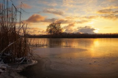 Günbatımı gökyüzü ve donmuş nehir kış manzarası.