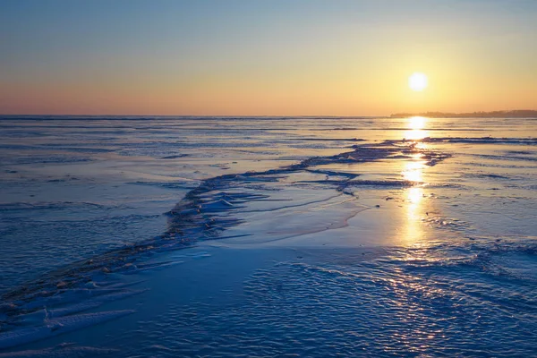Paisaje invernal con lago congelado, grietas y cielo al atardecer . — Foto de Stock