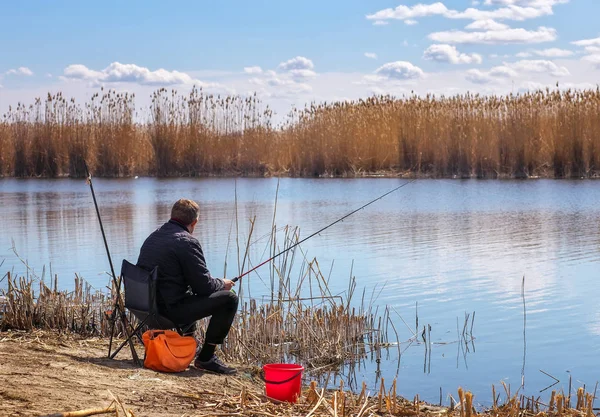 Un pescador con una caña de pescar sentado en una silla en la orilla del río — Foto de Stock