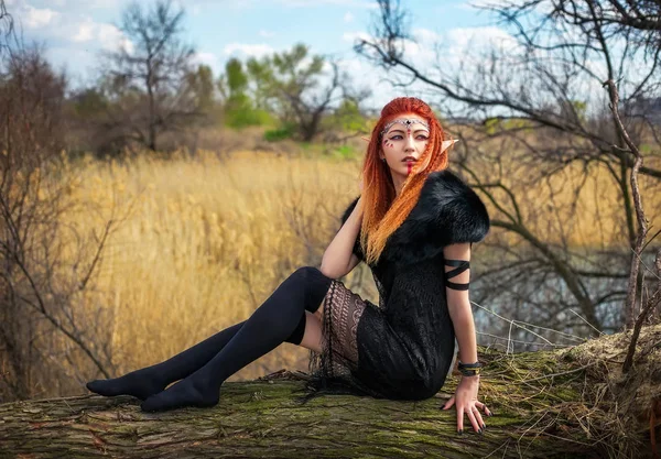 Elf vrouw met vurige haren op een logboek. — Stockfoto