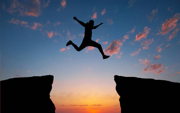 Man jumping across the gap from one rock to cling to the other. 