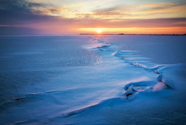 Vinterlandskap med frusen sjö, sprickor och solnedgång sky. — Stockfoto
