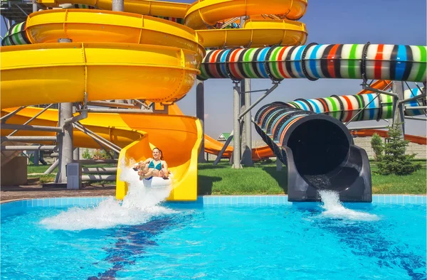 Girls go down from water slide to swimming pool in aqua park. — Stock Photo, Image