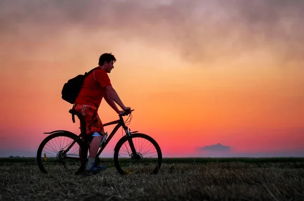 Байкер с велосипедом на поле во время восхода солнца — стоковое фото