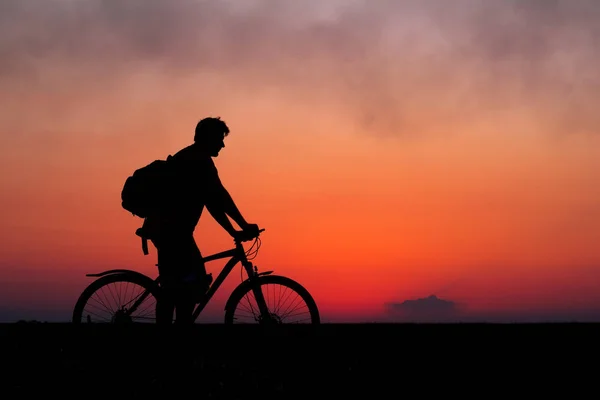 Силуэт велосипедиста на фоне красного заката. Байкер с велосипедом на поле во время восхода солнца — стоковое фото
