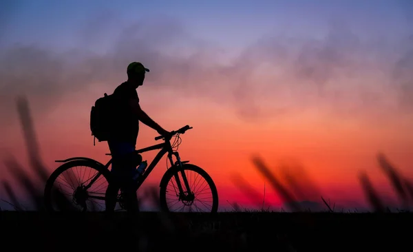 Silhuetten av cyklist på bakgrunden av röd solnedgång. Biker med cykel på fältet under sunrise — Stockfoto