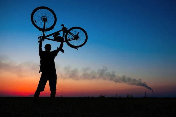 Silhuetten av cyklist på bakgrunden av röd solnedgång. Biker med cykel på fältet under sunrise — Stockfoto