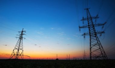 Elektrik direkleri ve yüksek gerilim elektrik hatları günbatımı sahasının silüeti.