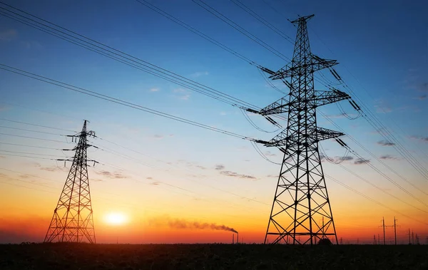 Silhouette of electricity pylons and high-voltage power lines on the field at sunset. — Stock Photo, Image