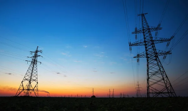 Silhouette of electricity pylons and high-voltage power lines on the field at sunset. — Stock Photo, Image