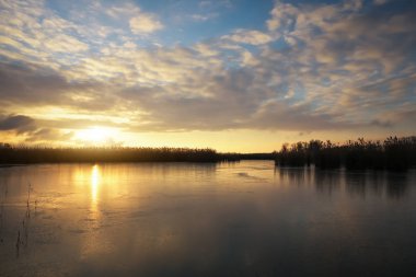 Donmuş nehir ve günbatımı gökyüzü ile kış manzarası.