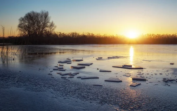 Zimní krajina s zamrzlou řeku, rákosí a západu slunce na obloze. — Stock fotografie