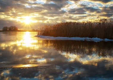 Kış manzara nehir, sazlık ve bulutlu gökyüzü günbatımı. 