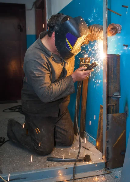 Worker with protective mask is welding a metal door. — Stock Photo, Image