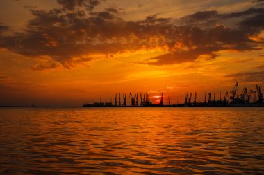 Güzel manzara ile ateşli günbatımı gökyüzü ve deniz. Berdyansk Limanı gündoğumu sırasında. Vinçler siluetleri ateşli, turuncu ve kırmızı gökyüzü karşı. 