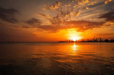 Güzel manzara ile ateşli günbatımı gökyüzü ve deniz. Berdyansk Limanı gündoğumu sırasında. Vinçler siluetleri ateşli, turuncu ve kırmızı gökyüzü karşı. 