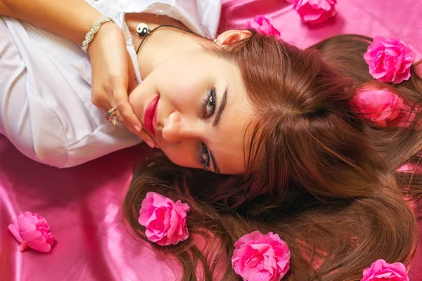 Mujer joven acostada sobre fondo rosa con flores . —  Fotos de Stock