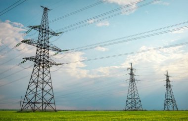 Güneşli bir günde mavi gökyüzünde bulutlar olan düz ve yeşil tarım arazisindeki yüksek voltaj hatları ve elektrik direkleri. Bulutlu ve yağmurlu. Buğday büyüyor.