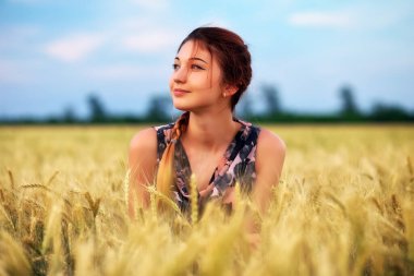 Gün batımında buğday tarlasında sevimli çekici bir genç kız. Düşünceli bir bakış. Romantik atmosfer.