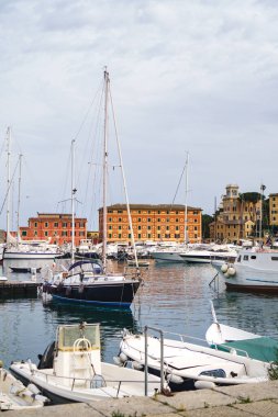Beyaz lüks yatların panoramik manzarası ve Santa Margherita Ligure limanında demirlemiş yelkenli tekneler, İtalyan Rivierası. Bulutlu mavi gökyüzü ile güzel Akdeniz manzarası.