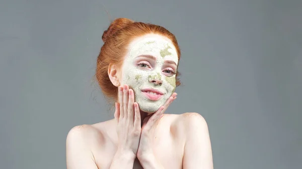 Beauty treatment. The girl applying a green clay mask for the face. aesthetic procedure