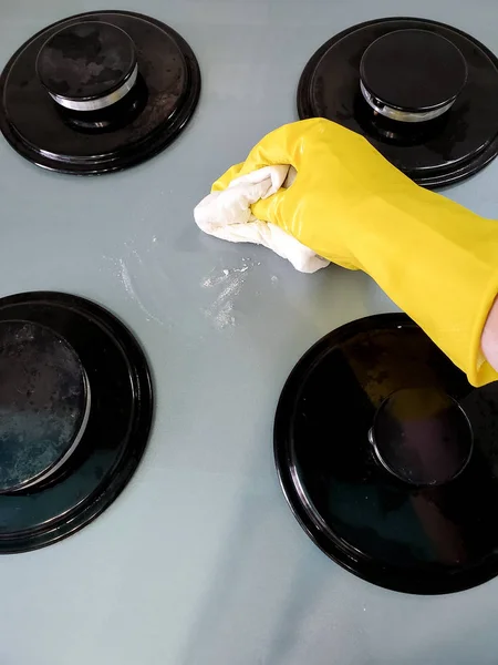 Hand in protective gloves cleans the gas stove with a rag