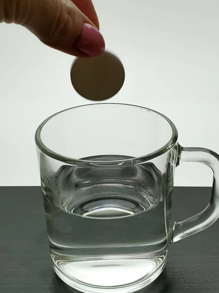 female hand throws the medicine into a glass of water close-up