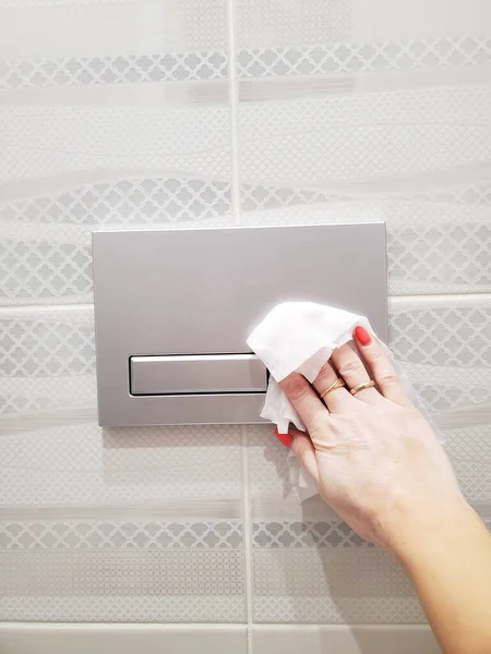 Womans hand wipes and disinfects the toilet flush button. Prevention of the spread of coronavirus