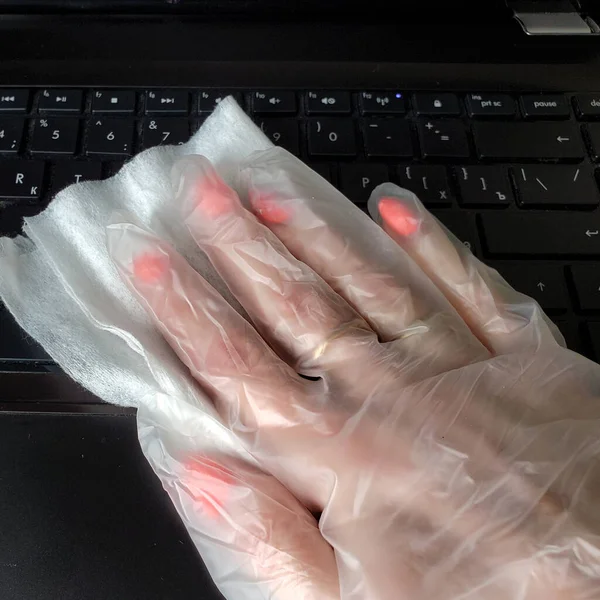 Close-up of a womans gloved hand disinfecting a keyboard and computer mouse, in order to prevent the spread of coronavirus