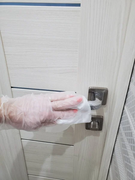 Womans hand wipes the door handles in an apartment with a disinfecting cloth to prevent the spread of coronavirus