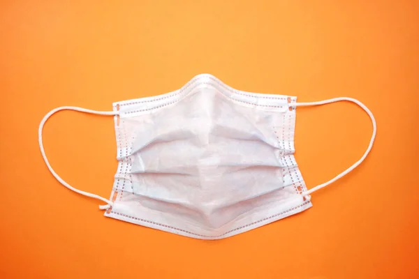 Dirty old medical mask, old face mask on an isolated orange background