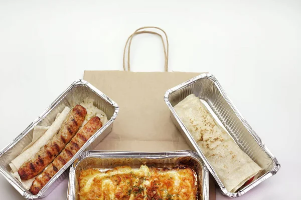 Delicious food in foil boxes, food delivery in a paper bag